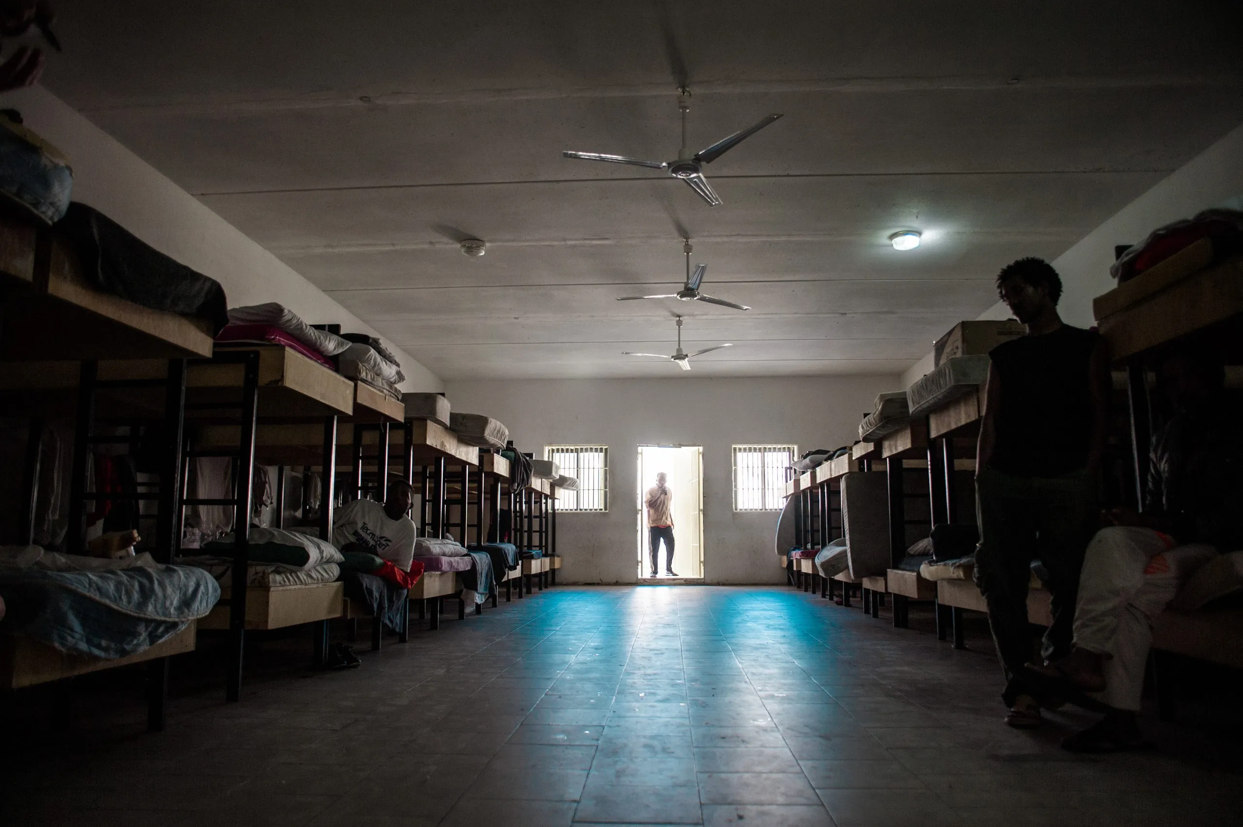 A long dormitory of bunk beds with ceiling fans inside the housing hangar at the Malta detention centre.