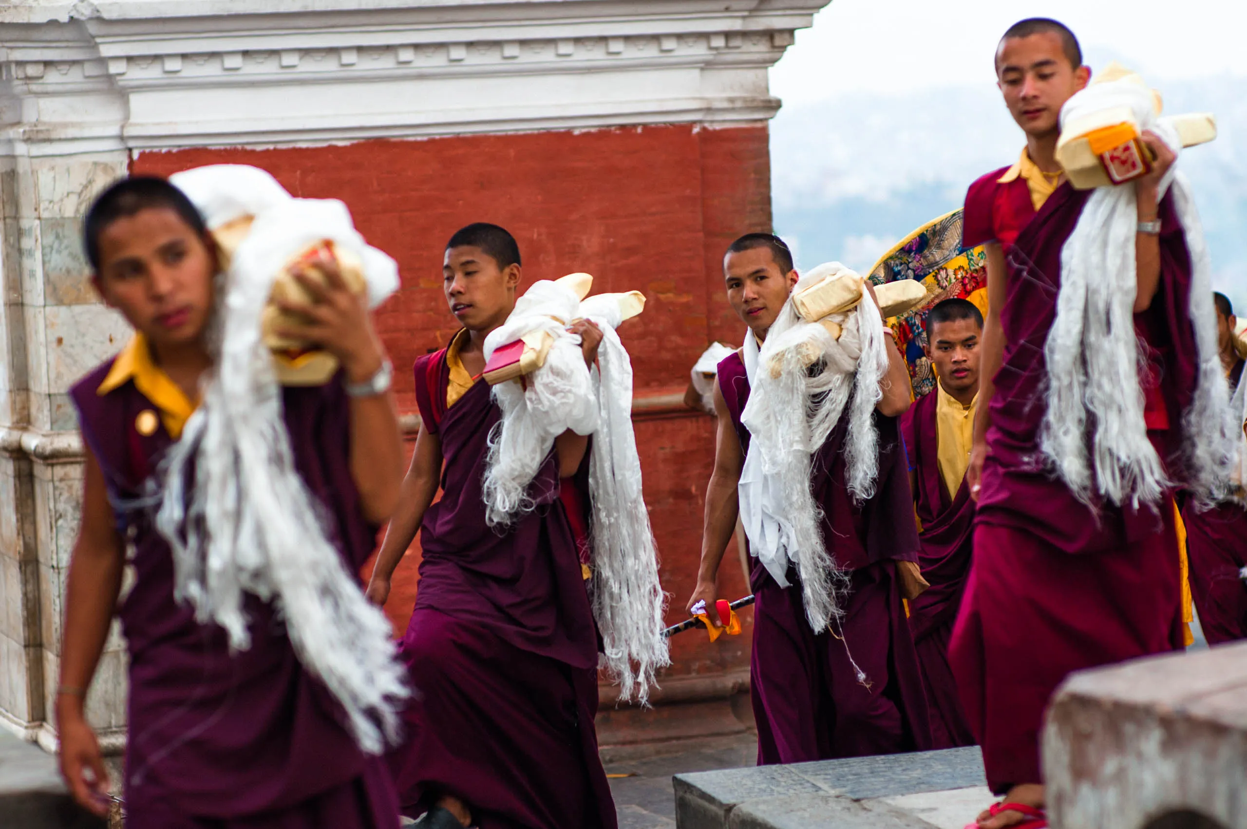 Young monks carry white khata scarves and butter-lamp packages along the temple terrace at Swayambhunath.