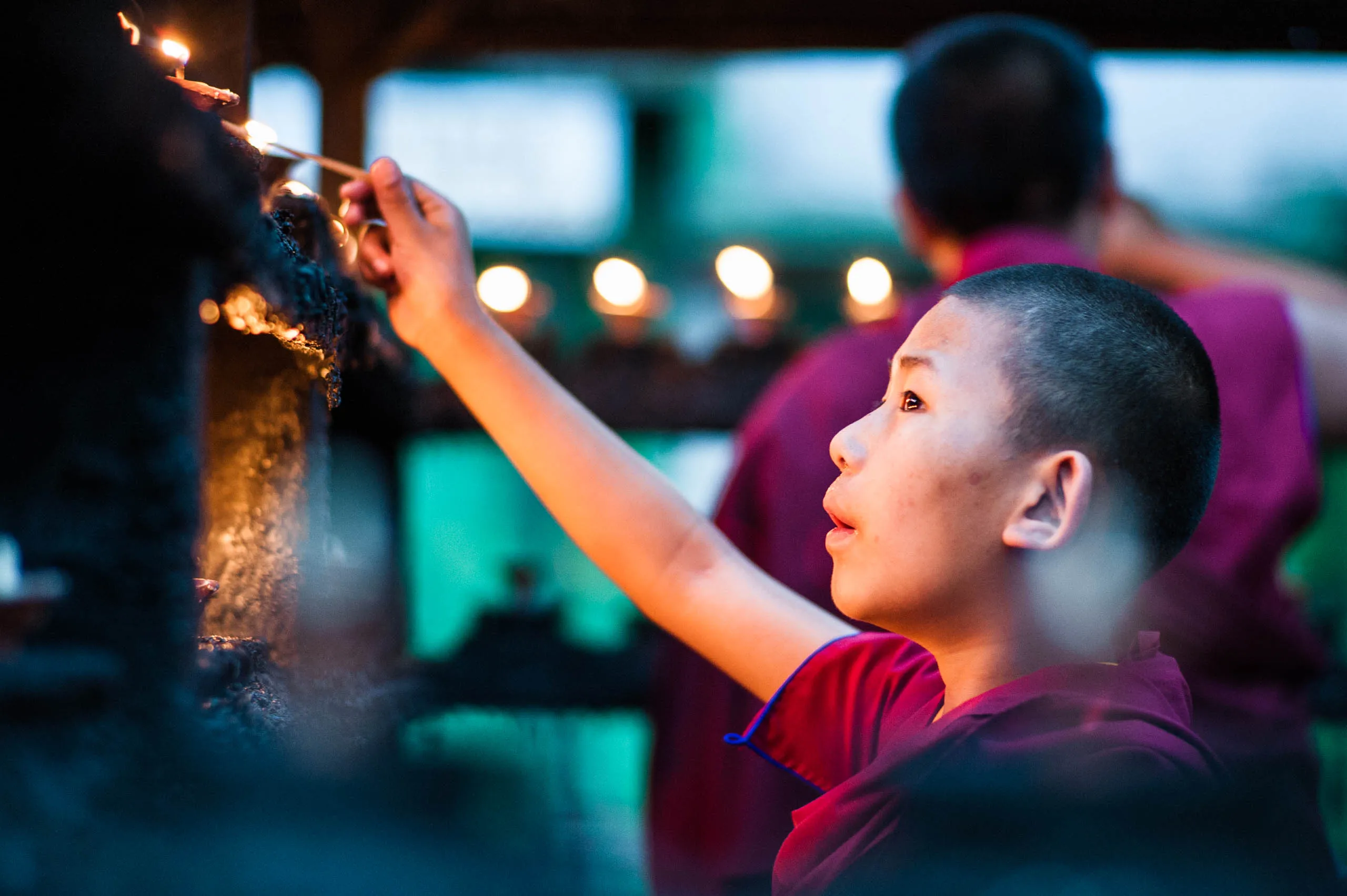 A close view of a young monk pouring oil into a row of small clay butter lamps at the temple in Kathmandu.