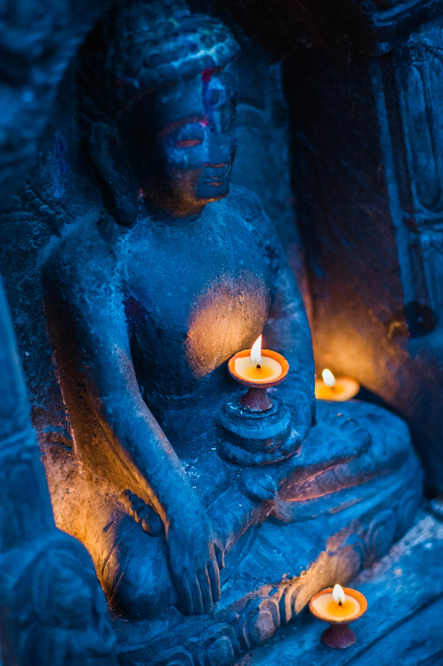 A small Buddha statue glows by butter-lamp flames in the deep blue twilight at Swayambhunath, Nepal.