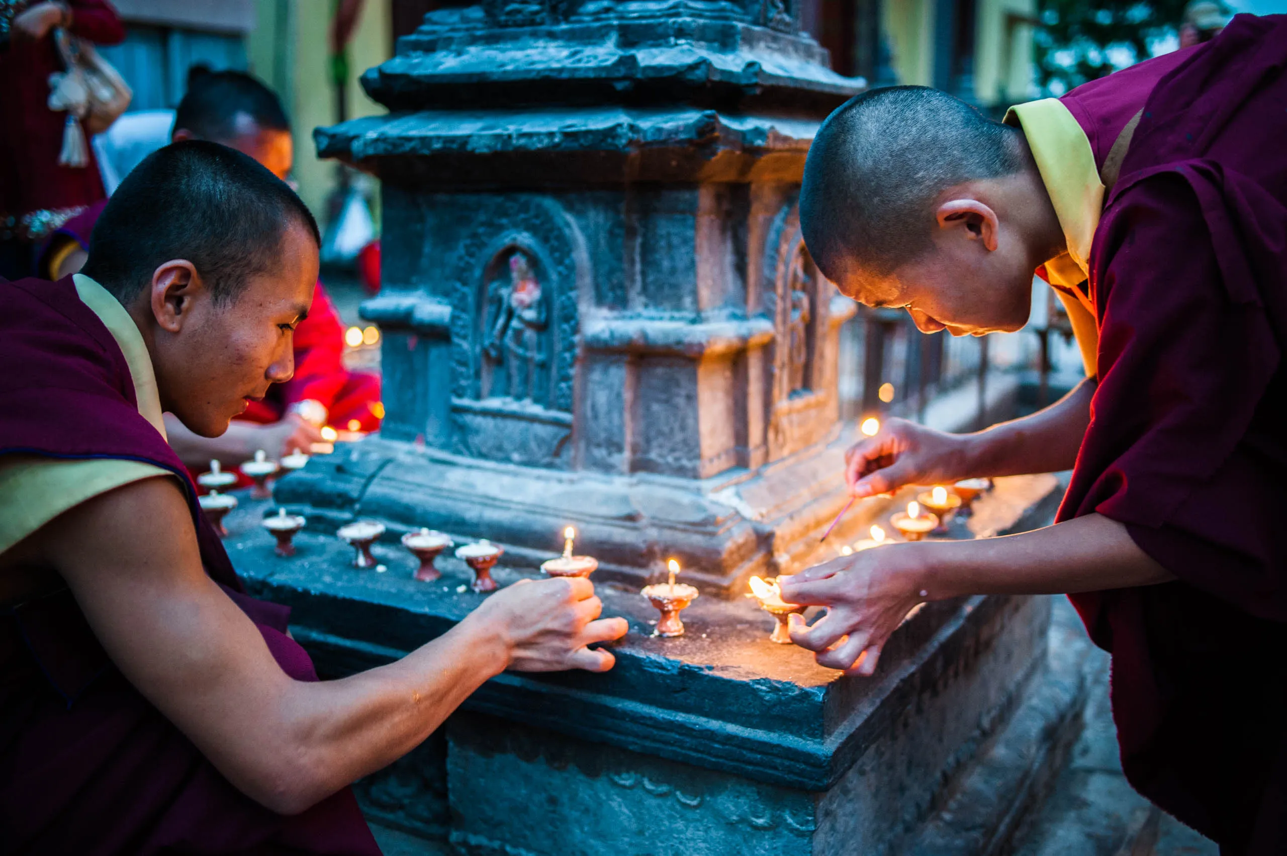 Two monks carefully light butter lamps around the base of a stupa at Swayambhunath, Kathmandu.