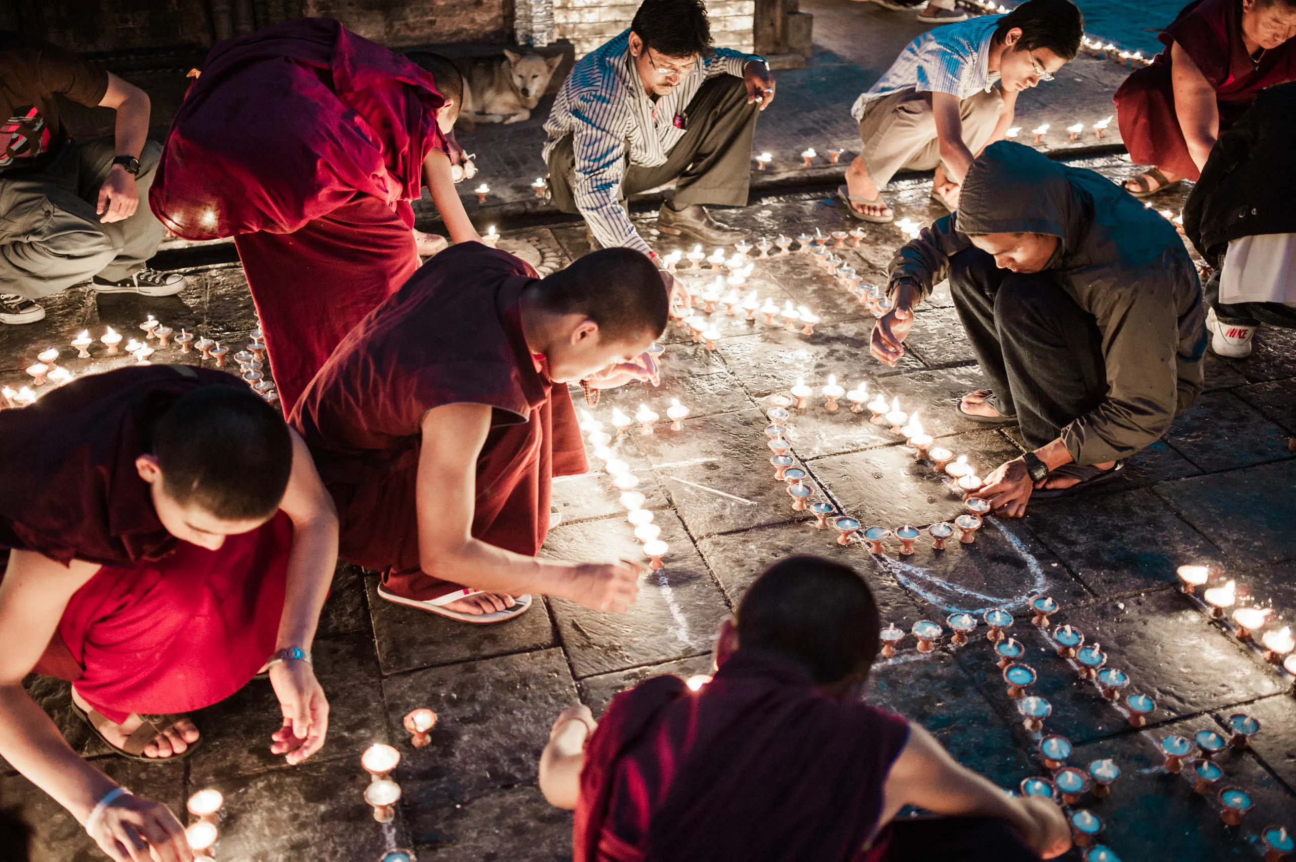 Monks and visitors crouch on the ground arranging butter lamps into the shape of a heart, at Swayambhunath.
