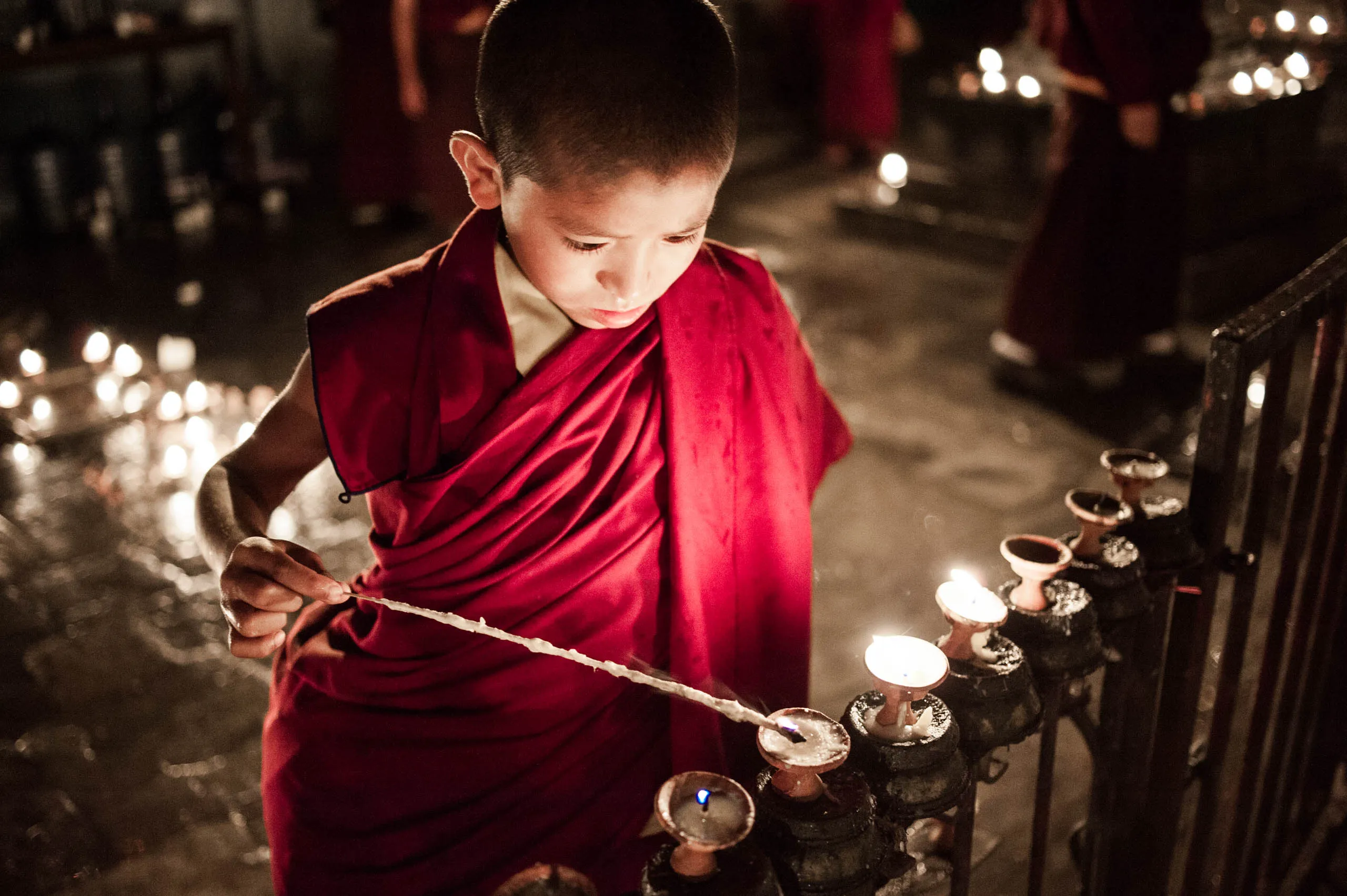 A young monk leans over a large basket of butter lamps to light them, at the Swayambhunath ceremony.
