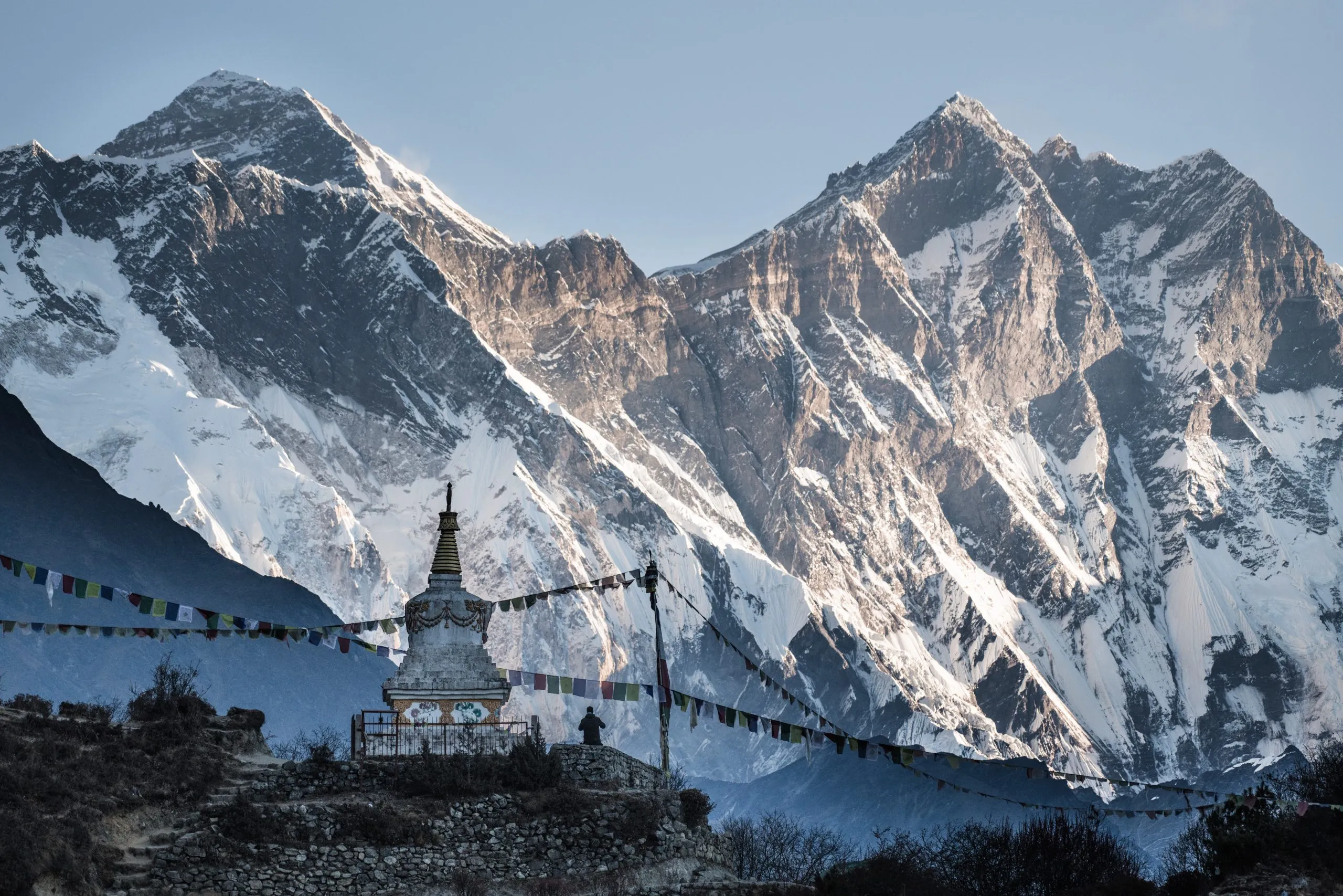 A whitewashed Buddhist stupa with prayer flags stands below the towering snow-and-rock face of Lhotse on the trail to Everest Base Camp.