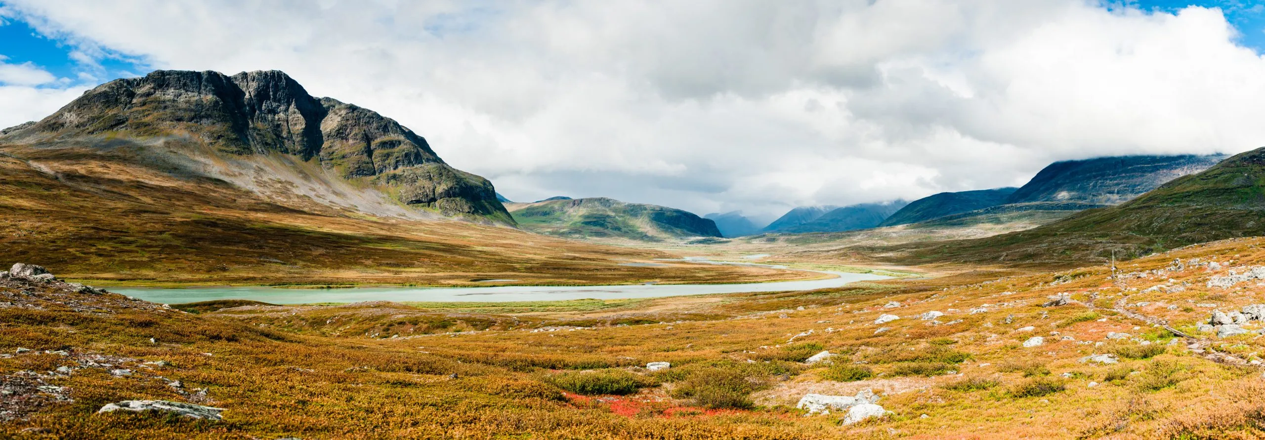 Panoramic landscape of a wide Swedish Lapland valley in autumn colours, a meandering river curving between low rocky peaks.