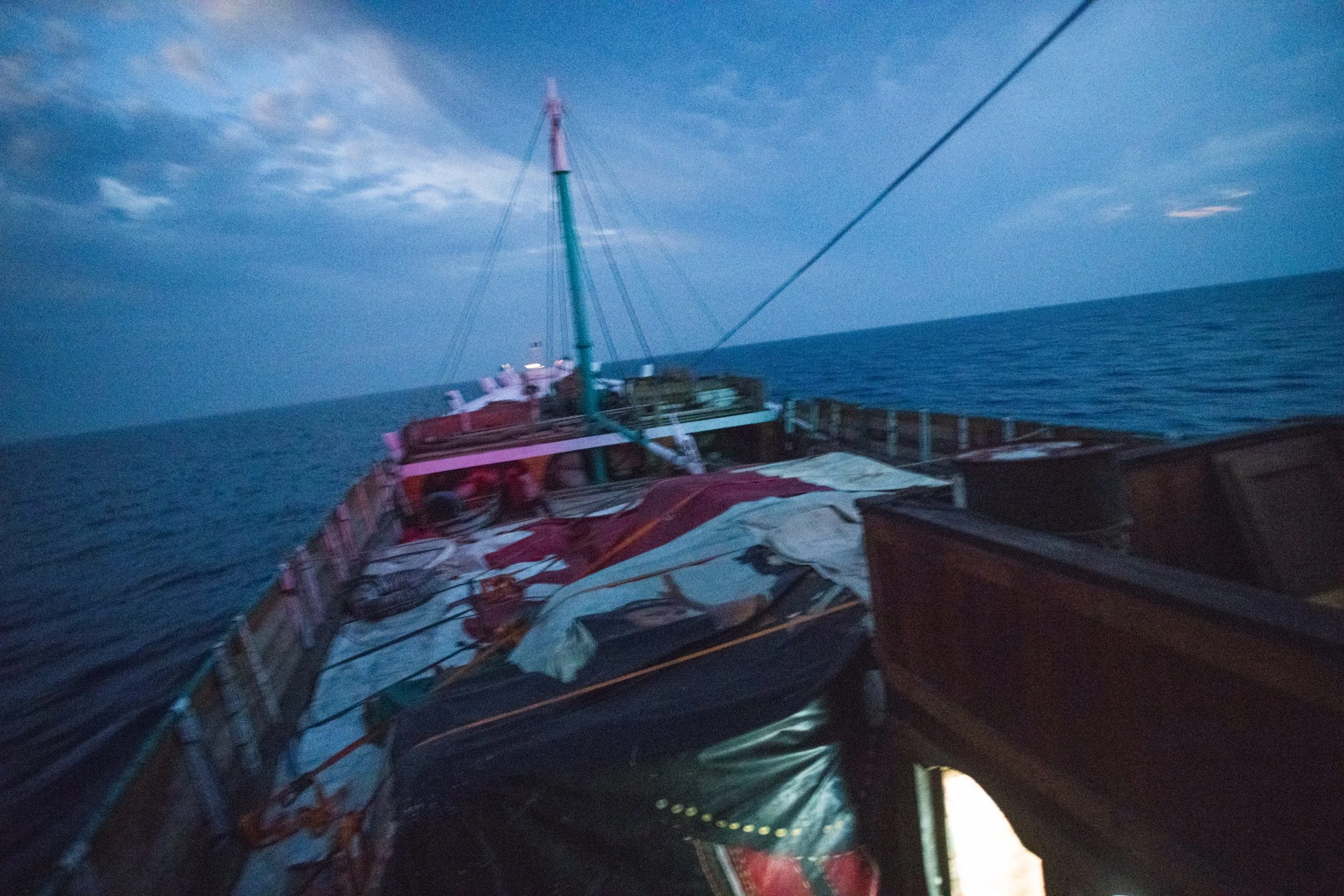 Bow of the wooden cargo dhow at sea at dusk, mast and rigging blurred by motion as it pitches in open swell on the way to Socotra.