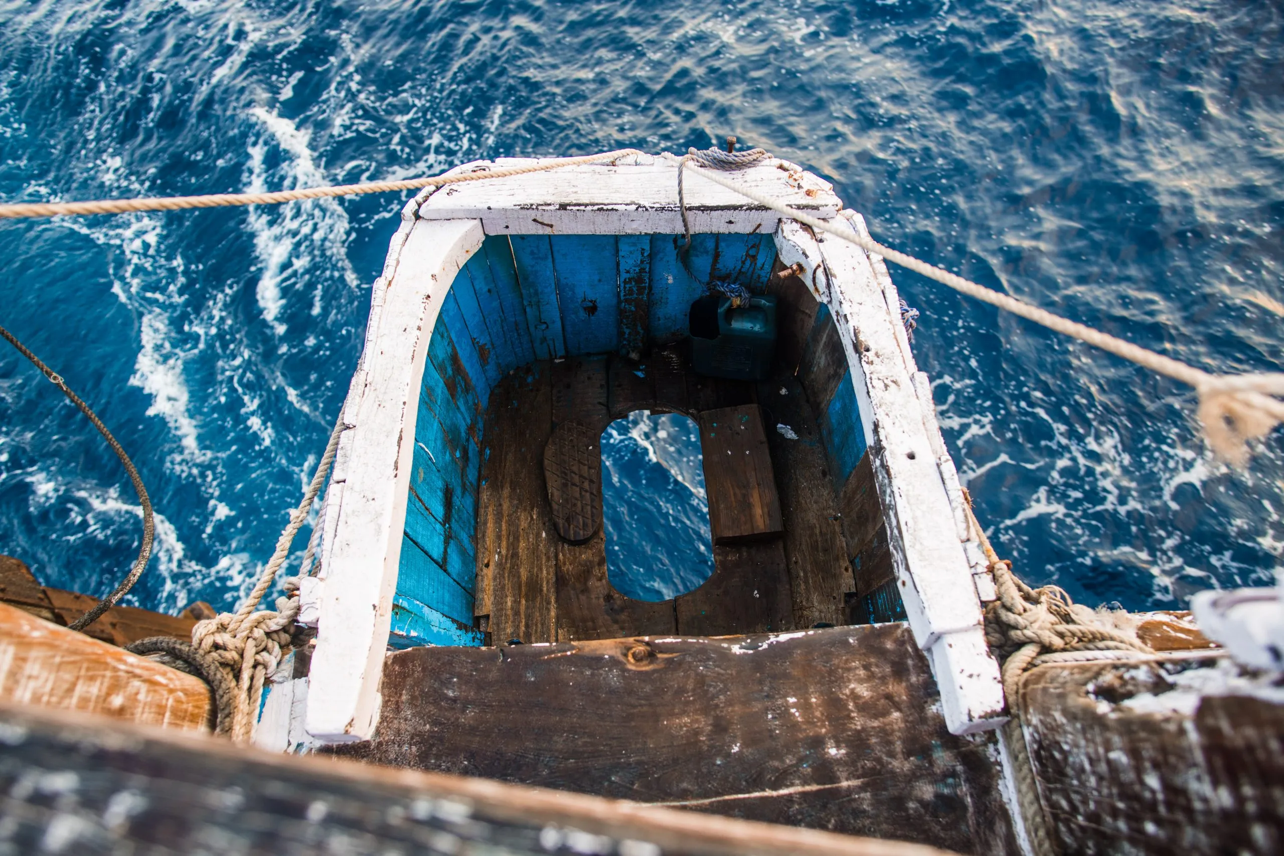 Looking down from the bow of the dhow at a small white-painted lookout perch over rough open water during the crossing.