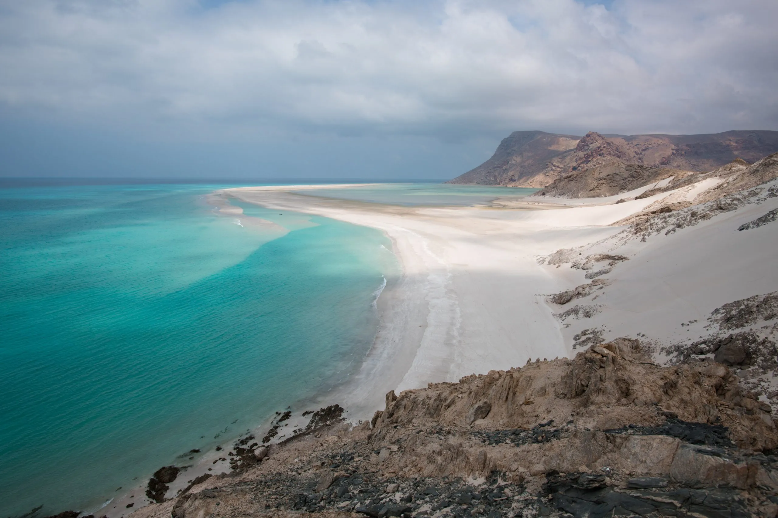 Cliff-top view of a long curving sandbar reaching into turquoise water at Detwah Lagoon on the western tip of Socotra.