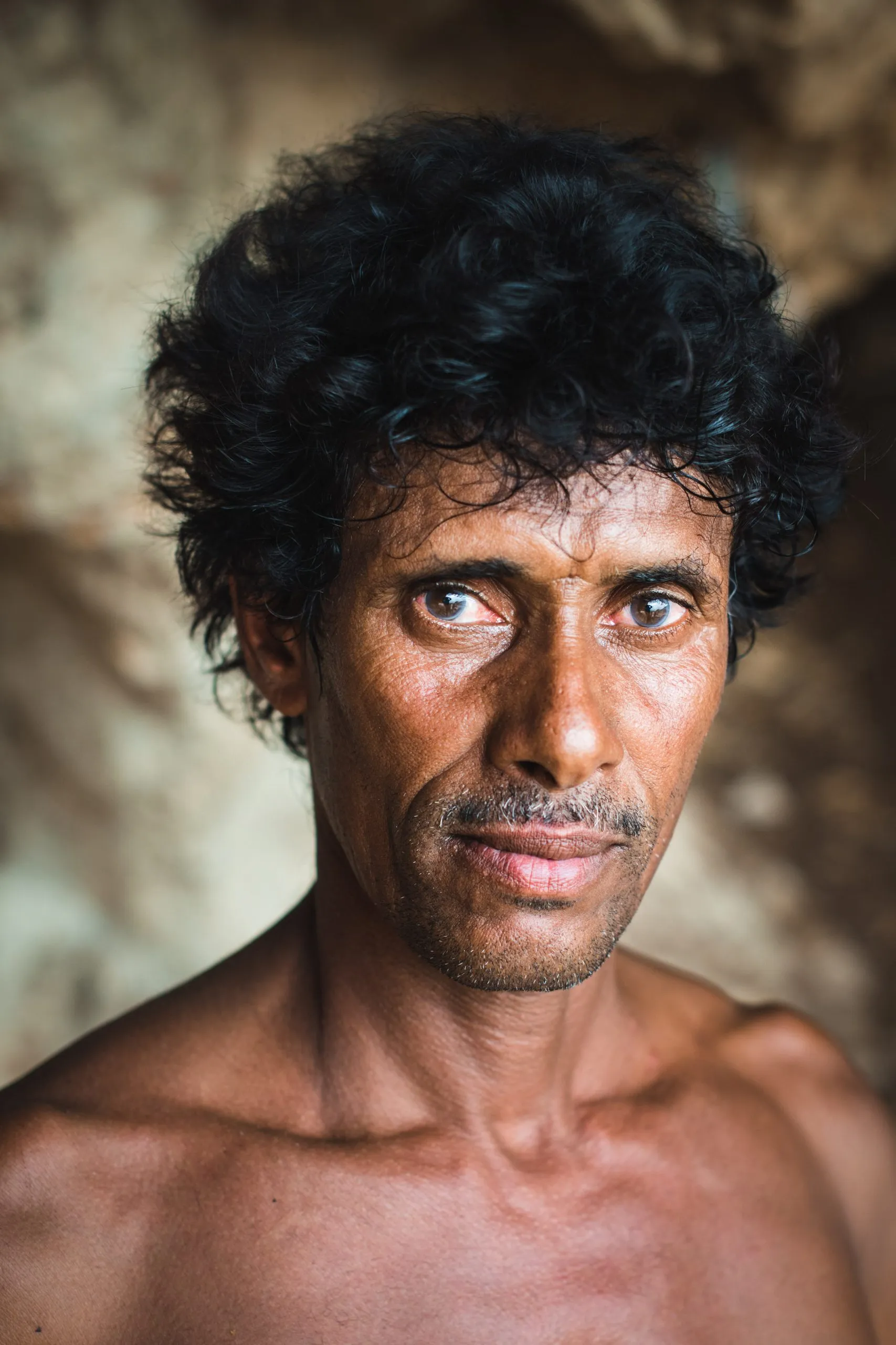 Close portrait of a Socotri man with curly black hair and bright eyes, photographed inside a cave dwelling.