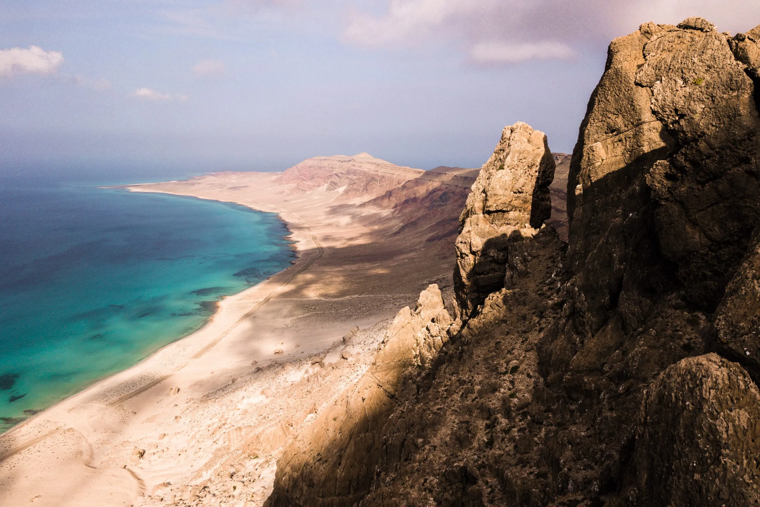 View from a rocky promontory over a long beach and turquoise sea curving toward distant headlands on Socotra.