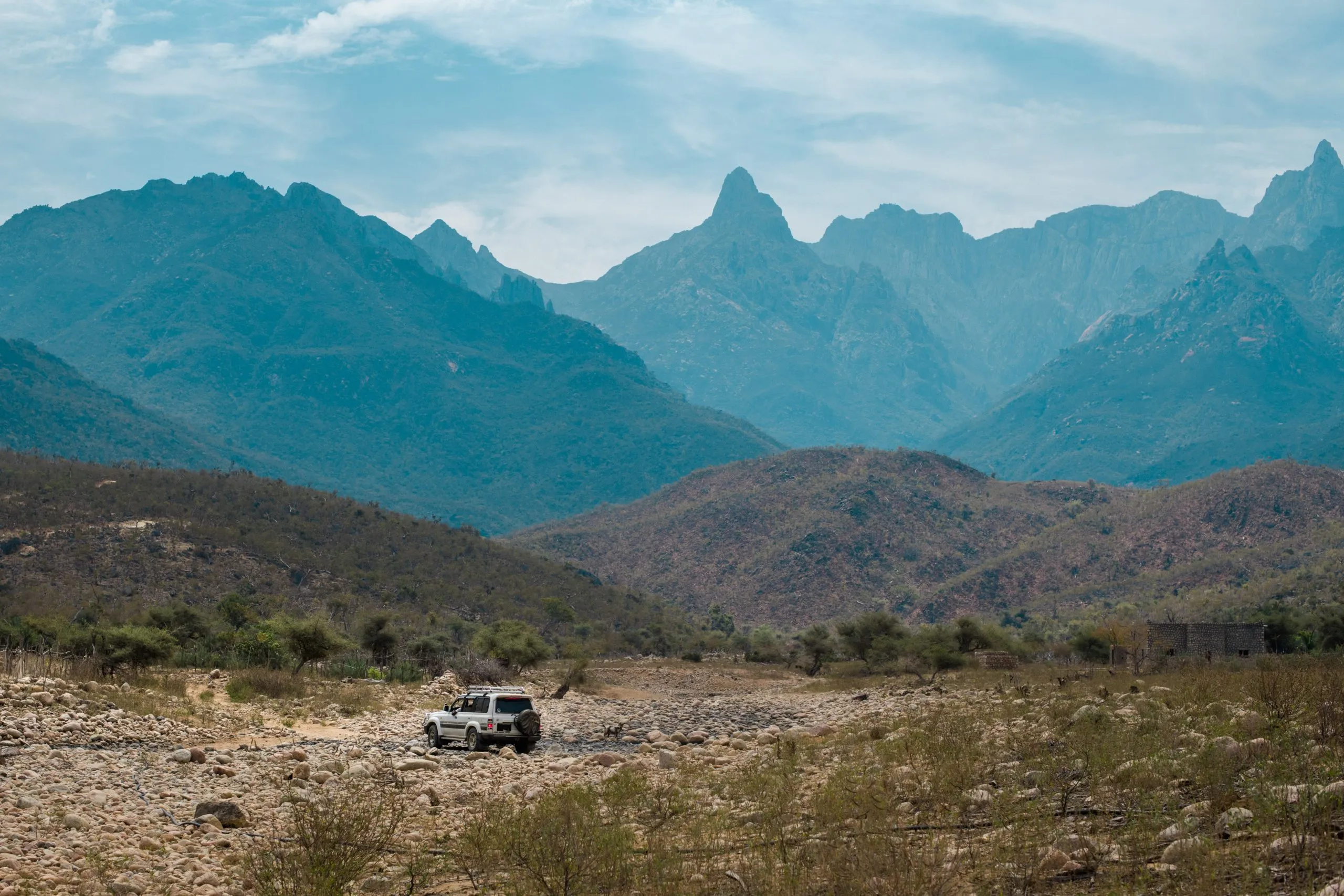 A four-wheel-drive parked in a dry stony riverbed below the dramatic spires of the Haghier Mountains.