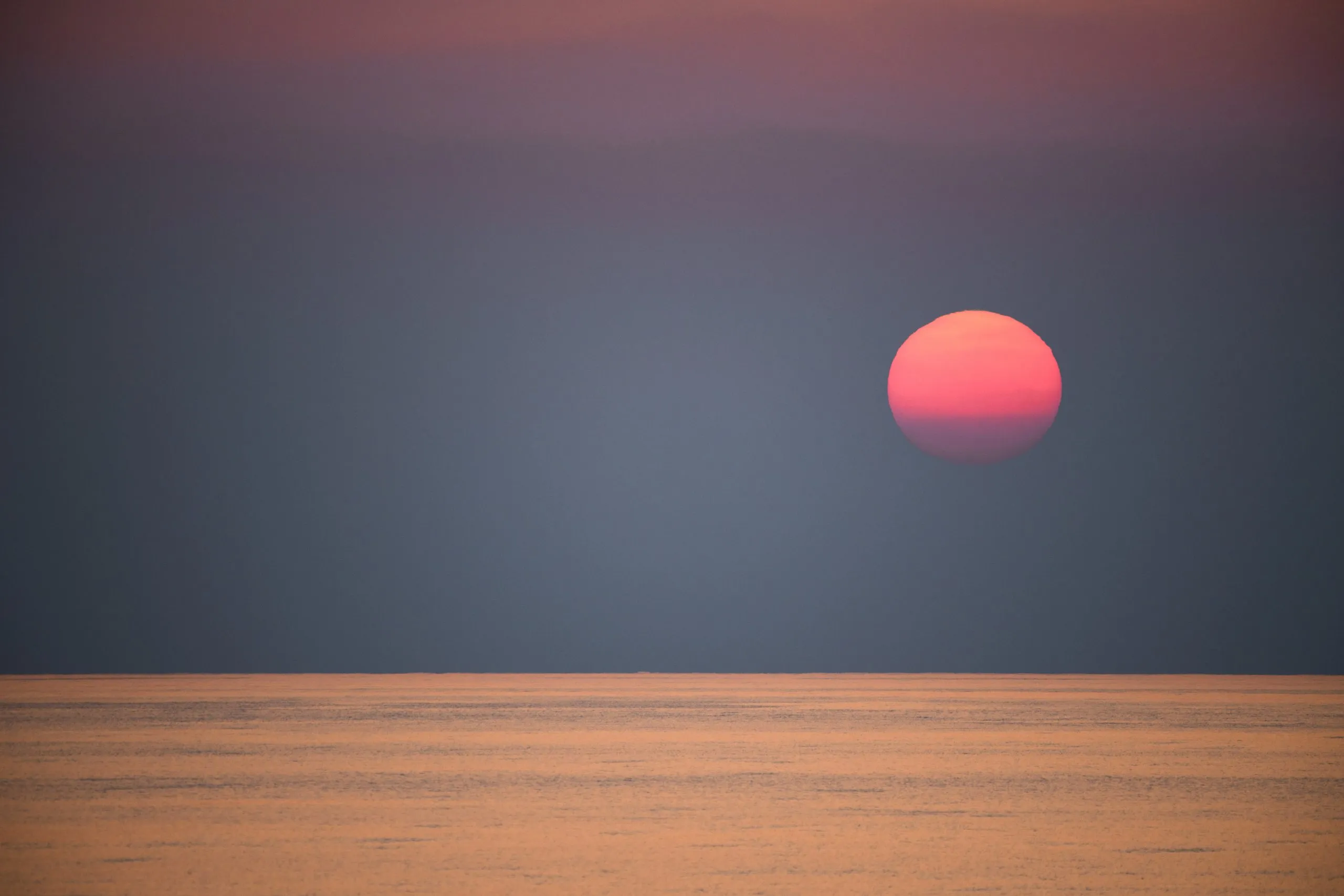 A large red sun sits low above a placid sea at dusk, gold light skimming the surface of the Arabian Sea on the return crossing from Socotra.